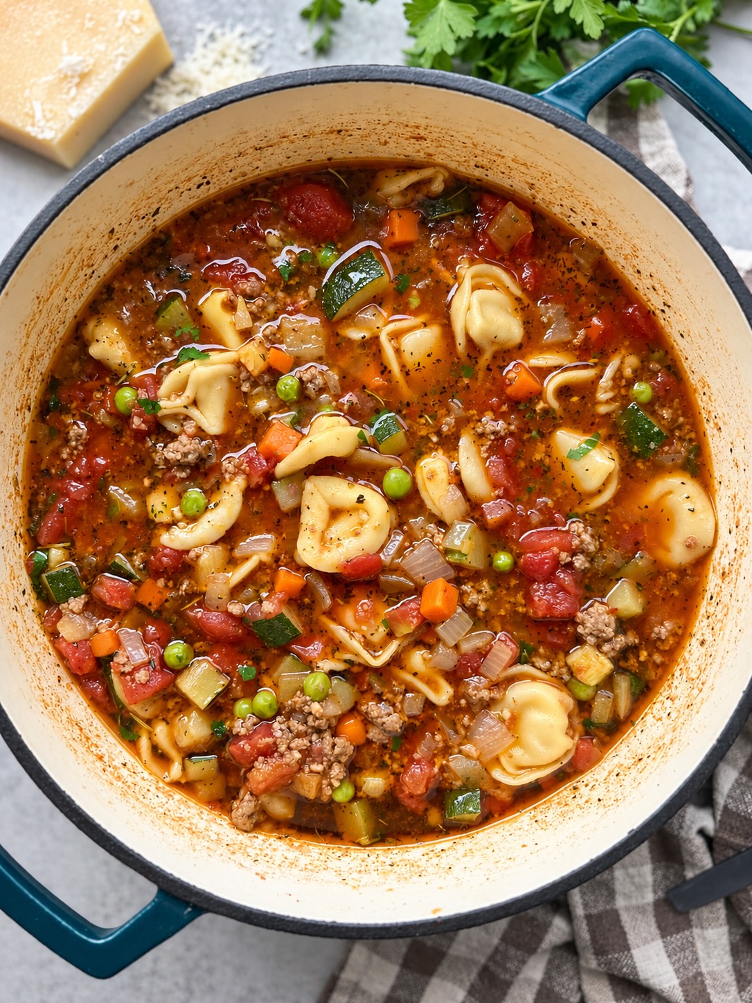 Beef and tortellini vegetable soup with cheese tortellini, zucchini, carrots, and peas in a blue Dutch oven.