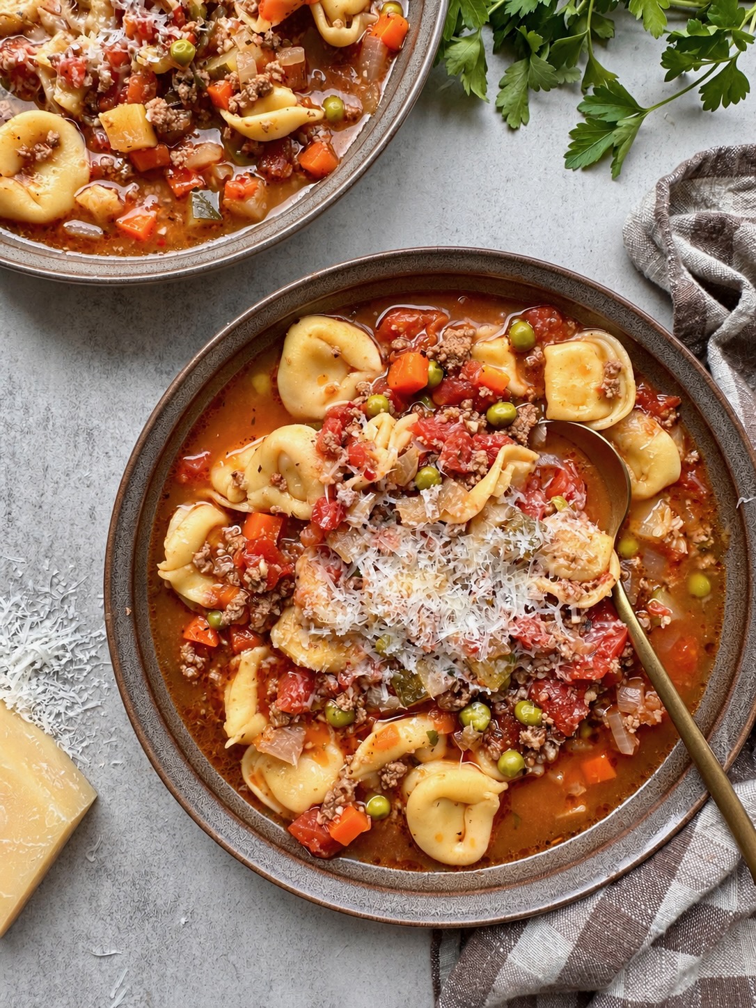 Beef and tortellini vegetable soup topped with grated Parmesan in a dark bowl.