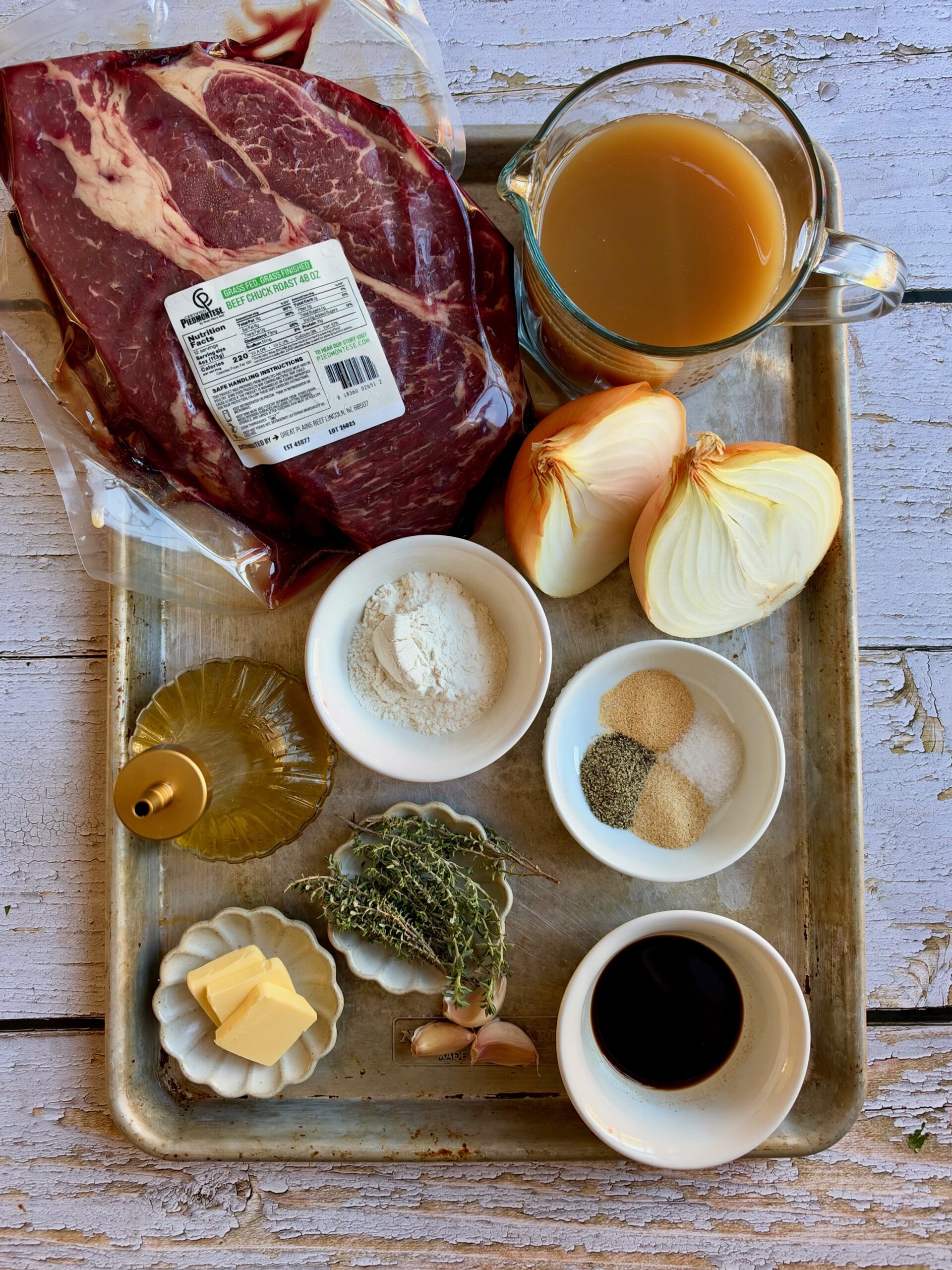 Ingredients for crockpot French onion pot roast on a tray, including chuck roast, yellow onions, beef bone broth, butter, Worcestershire, thyme, garlic, and seasonings.