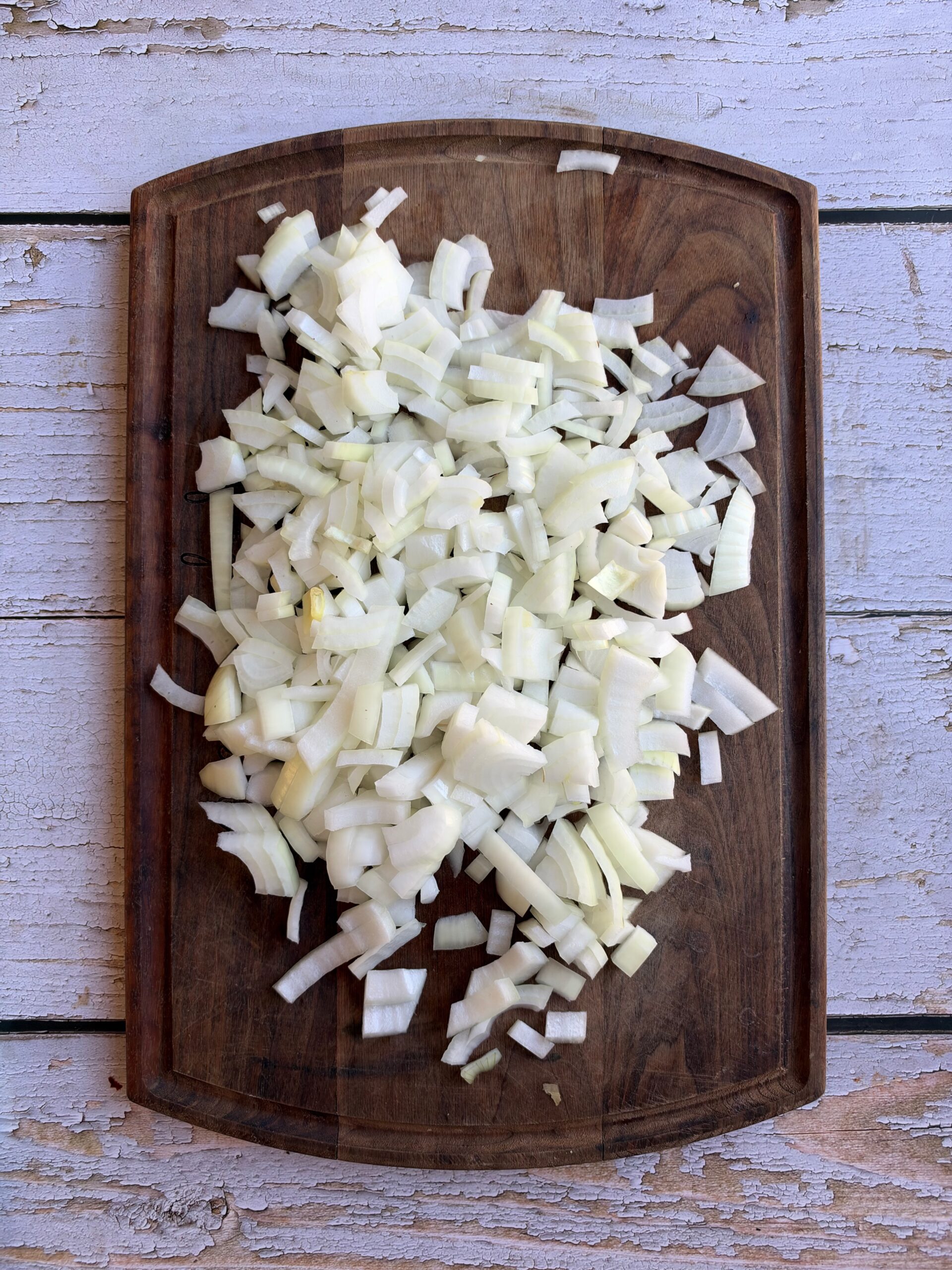 Diced yellow onions on a wooden cutting board.