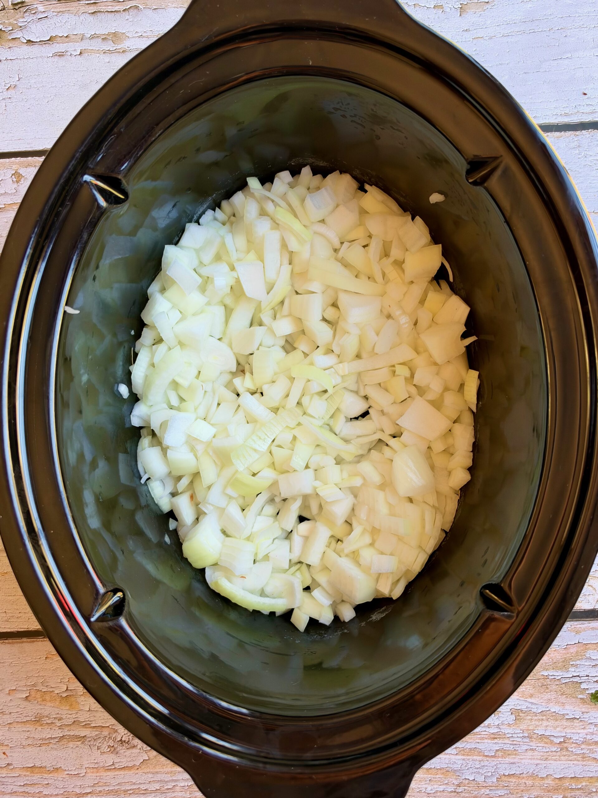 Diced yellow onions in the bottom of a slow cooker.