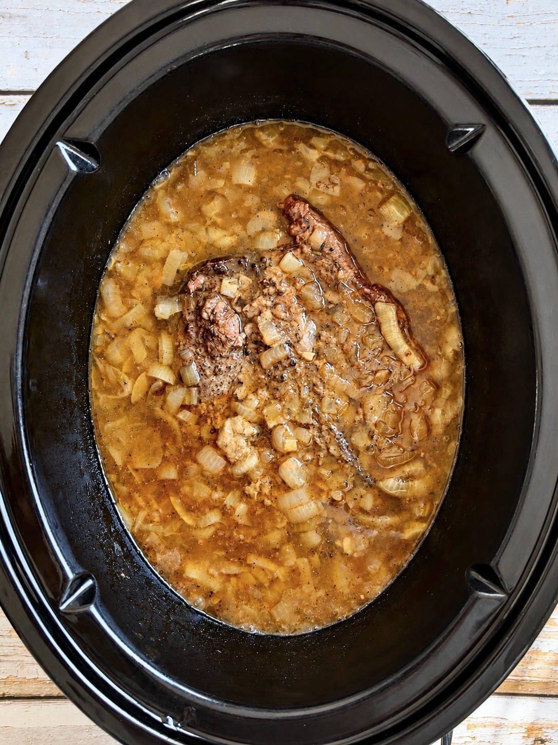 Chuck roast cooking in beef broth and onions in a slow cooker.