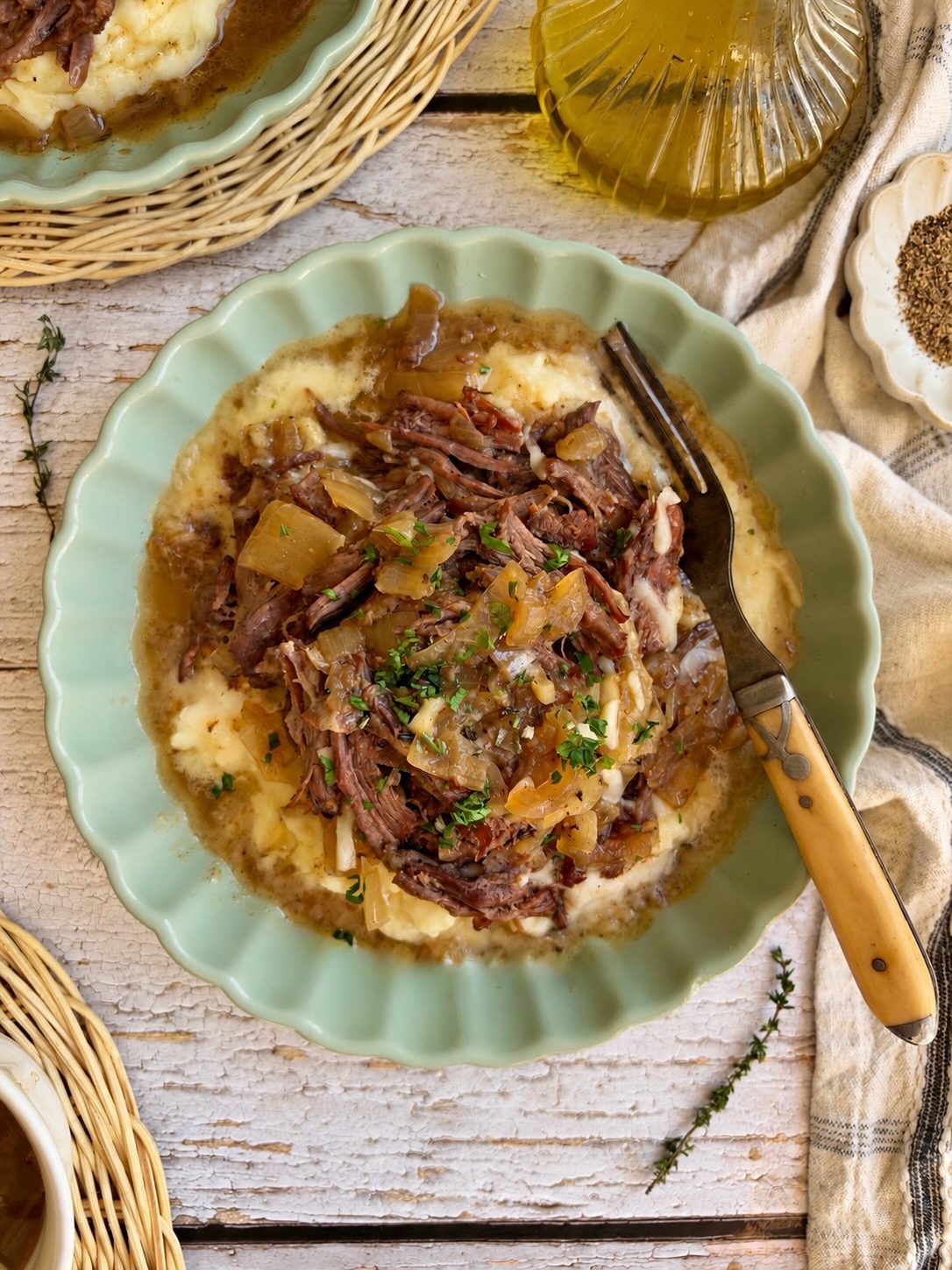 A bowl of French onion pot roast over mashed potatoes with a fork.