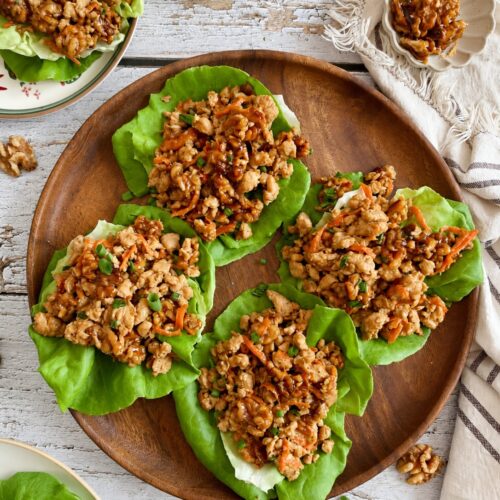 Four lettuce wraps filled with ground chicken and carrots, arranged on a wooden platter.