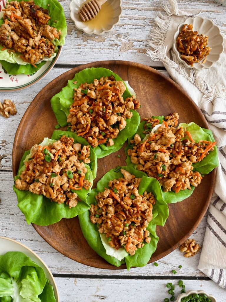 Four lettuce wraps filled with ground chicken and carrots, arranged on a wooden platter.