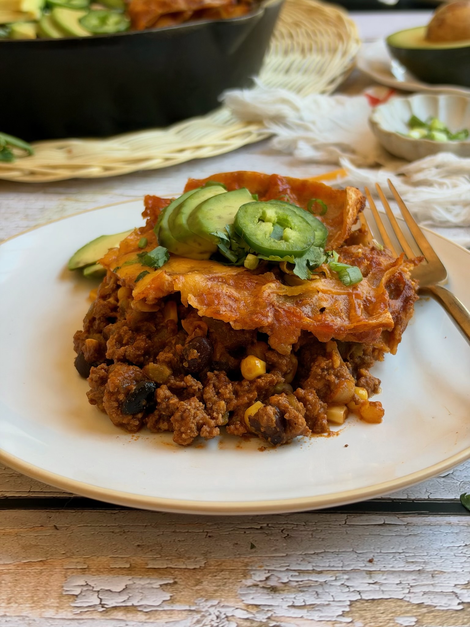 A serving of skillet beef enchiladas topped with avocado and jalapeño on a white plate.