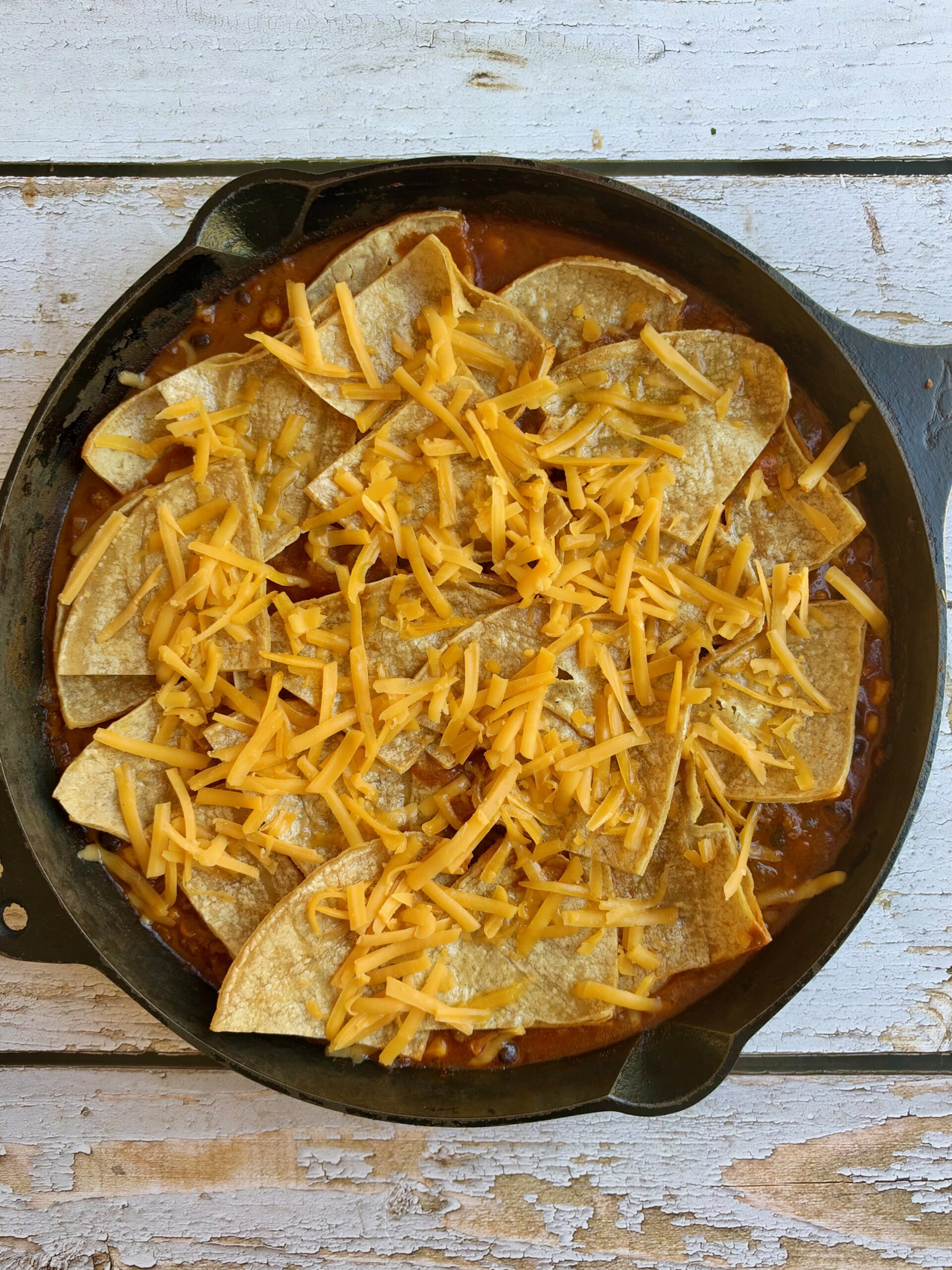 Shredded cheese sprinkled over corn tortilla wedges in a cast iron skillet before baking.