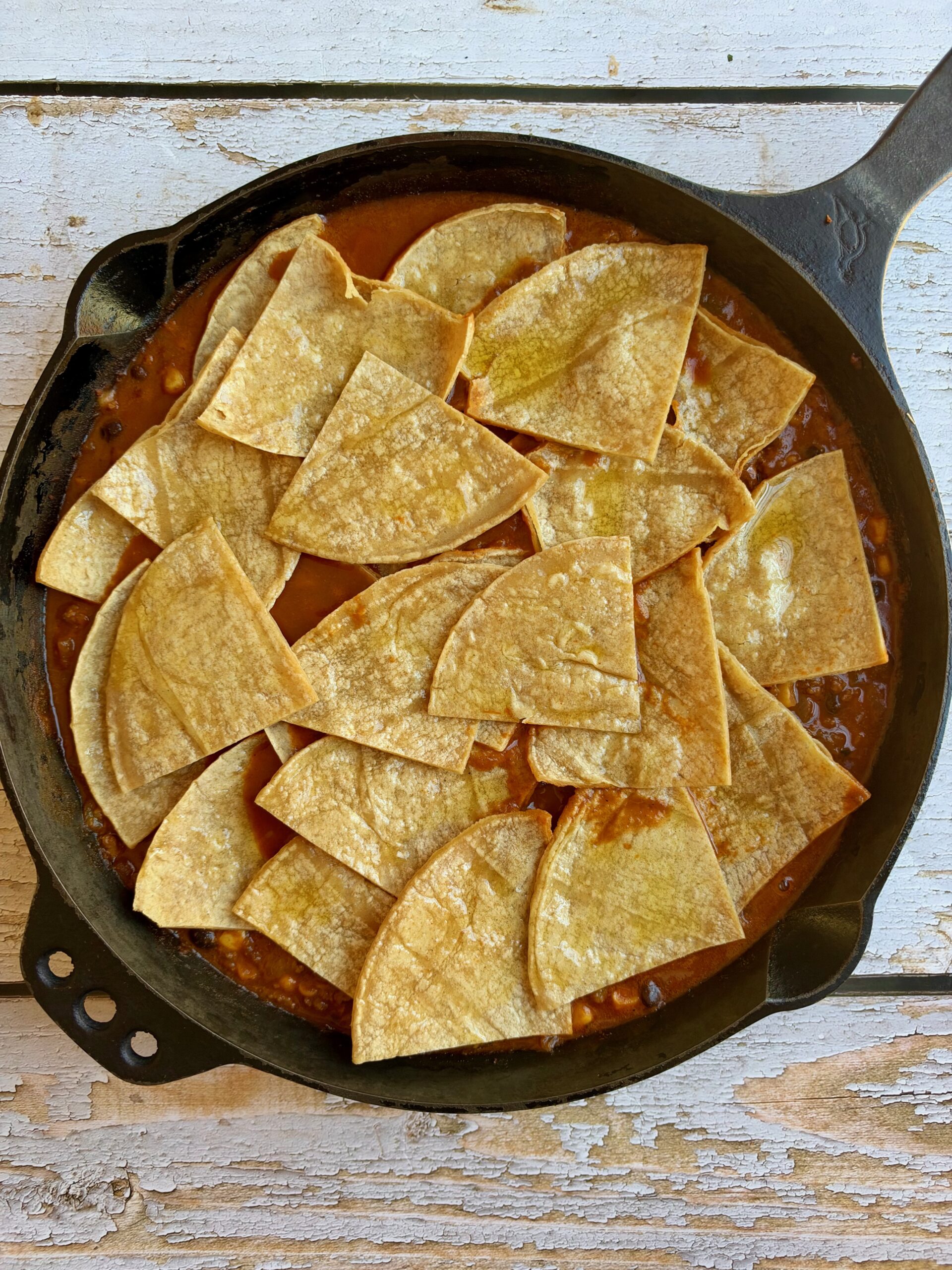 Corn tortilla wedges layered over the beef enchilada filling in a cast iron skillet.
