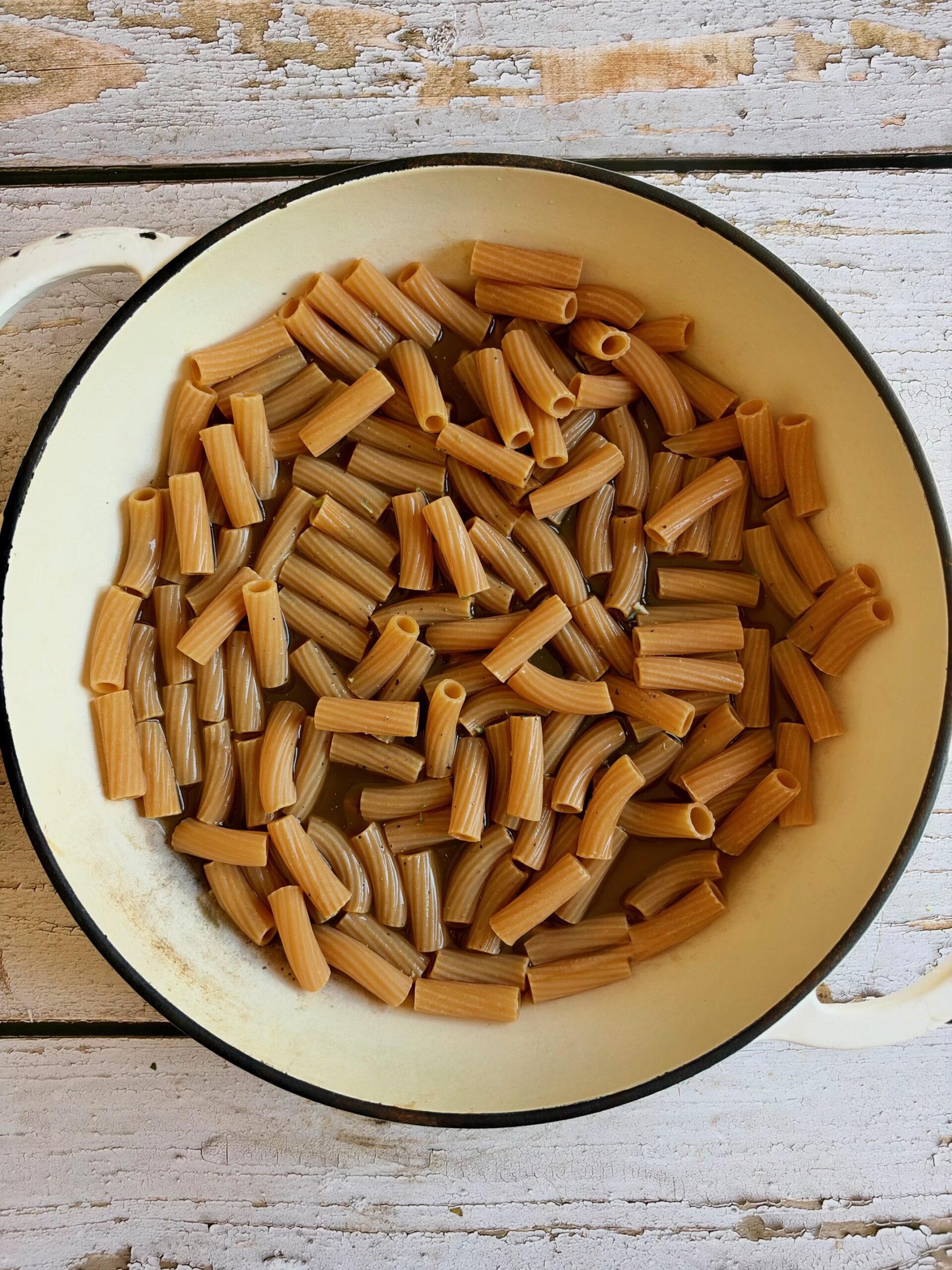Rigatoni pasta in a shallow cream-colored pan resting on a weathered white wooden surface.