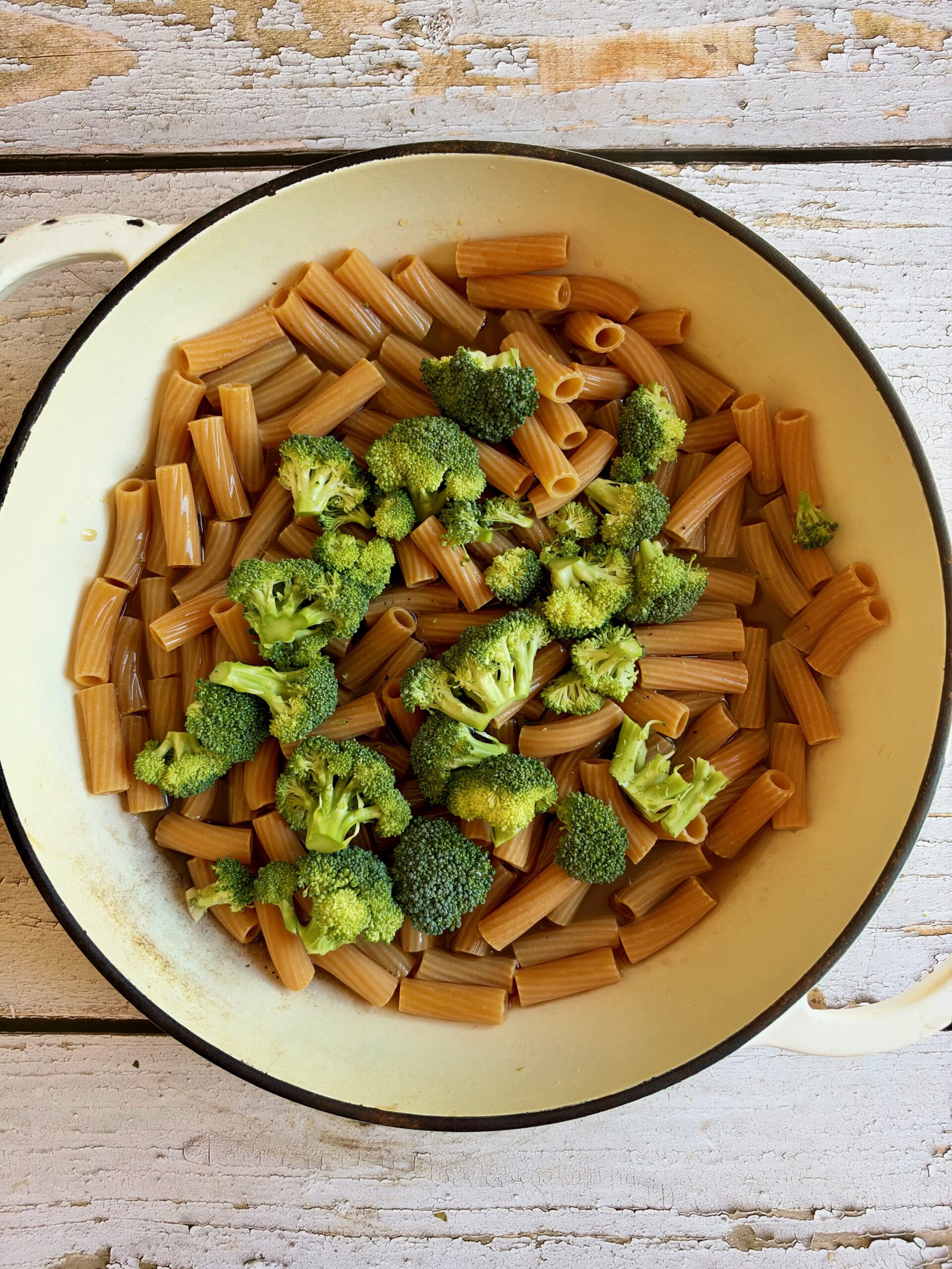 Rigatoni pasta with broccoli florets in a shallow enamel pan.
