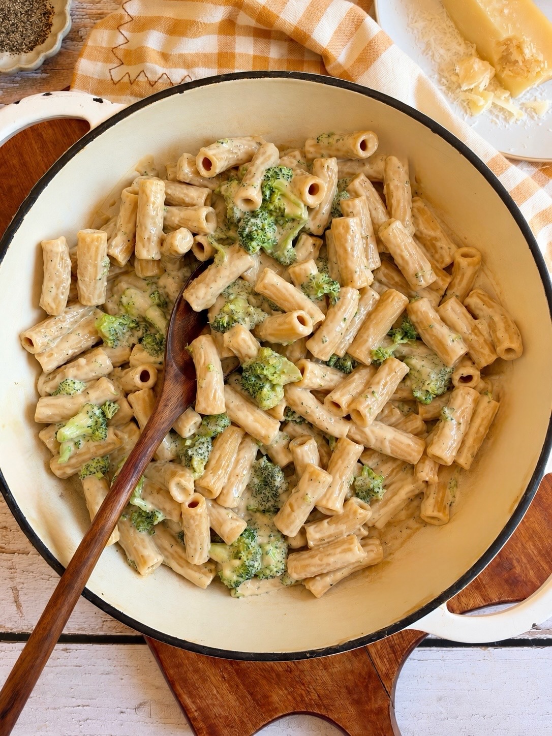Rigatoni pasta with broccoli in a creamy sauce inside a white enameled skillet with a wooden serving spoon.