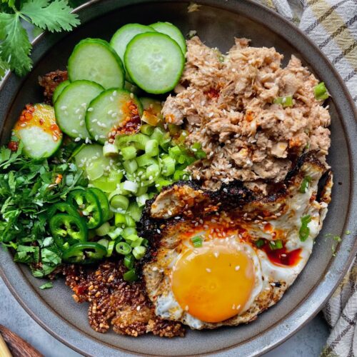 Spicy tuna crispy rice bowl topped with a fried egg, cucumber, jalapeño, green onions, cilantro, and chili crisp.