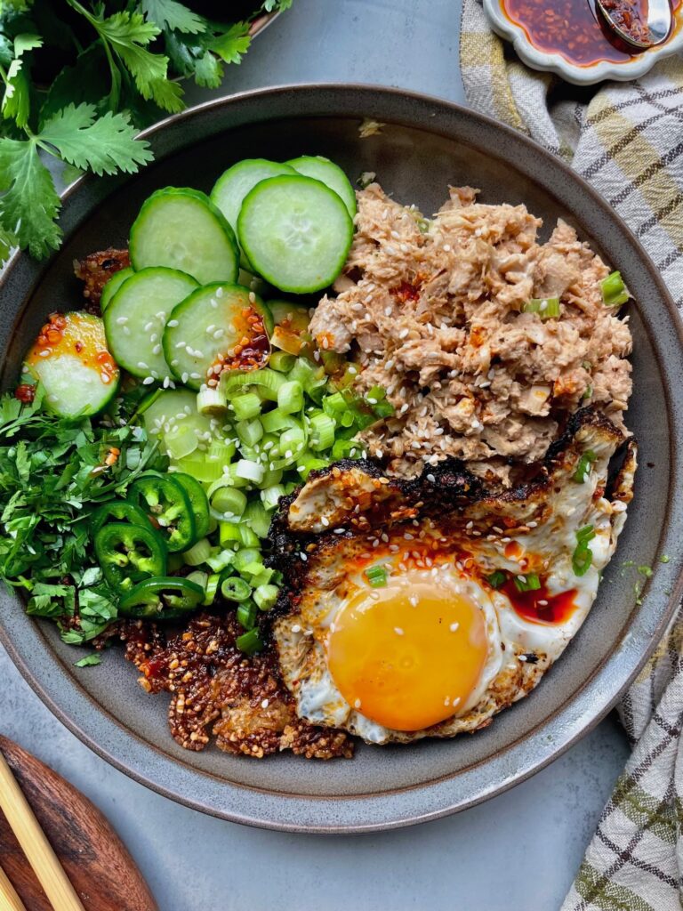 Spicy tuna crispy rice bowl topped with a fried egg, cucumber, jalapeño, green onions, cilantro, and chili crisp.