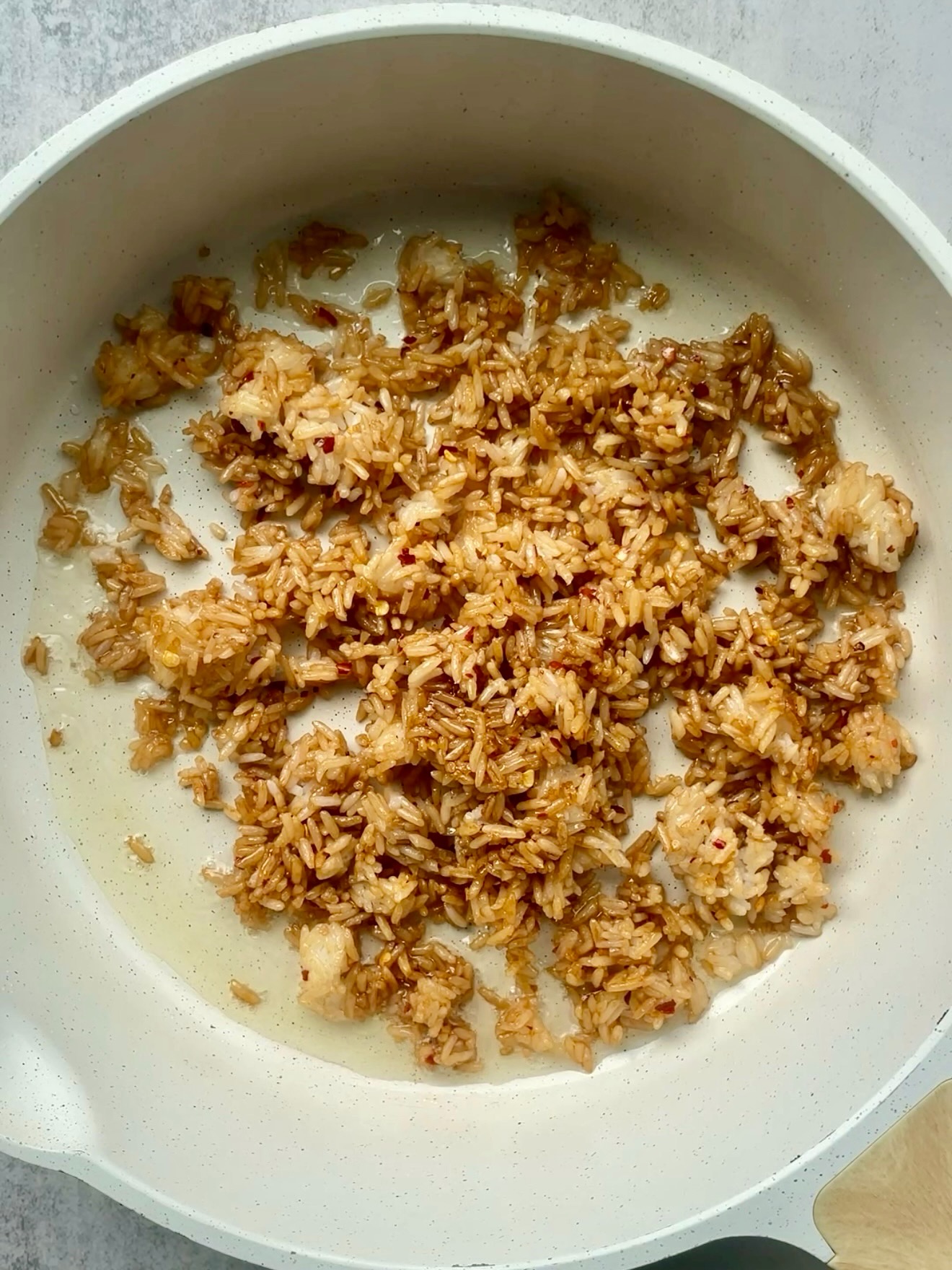Cooked rice tossed with tamari, sesame oil, and chili crisp in a white skillet.