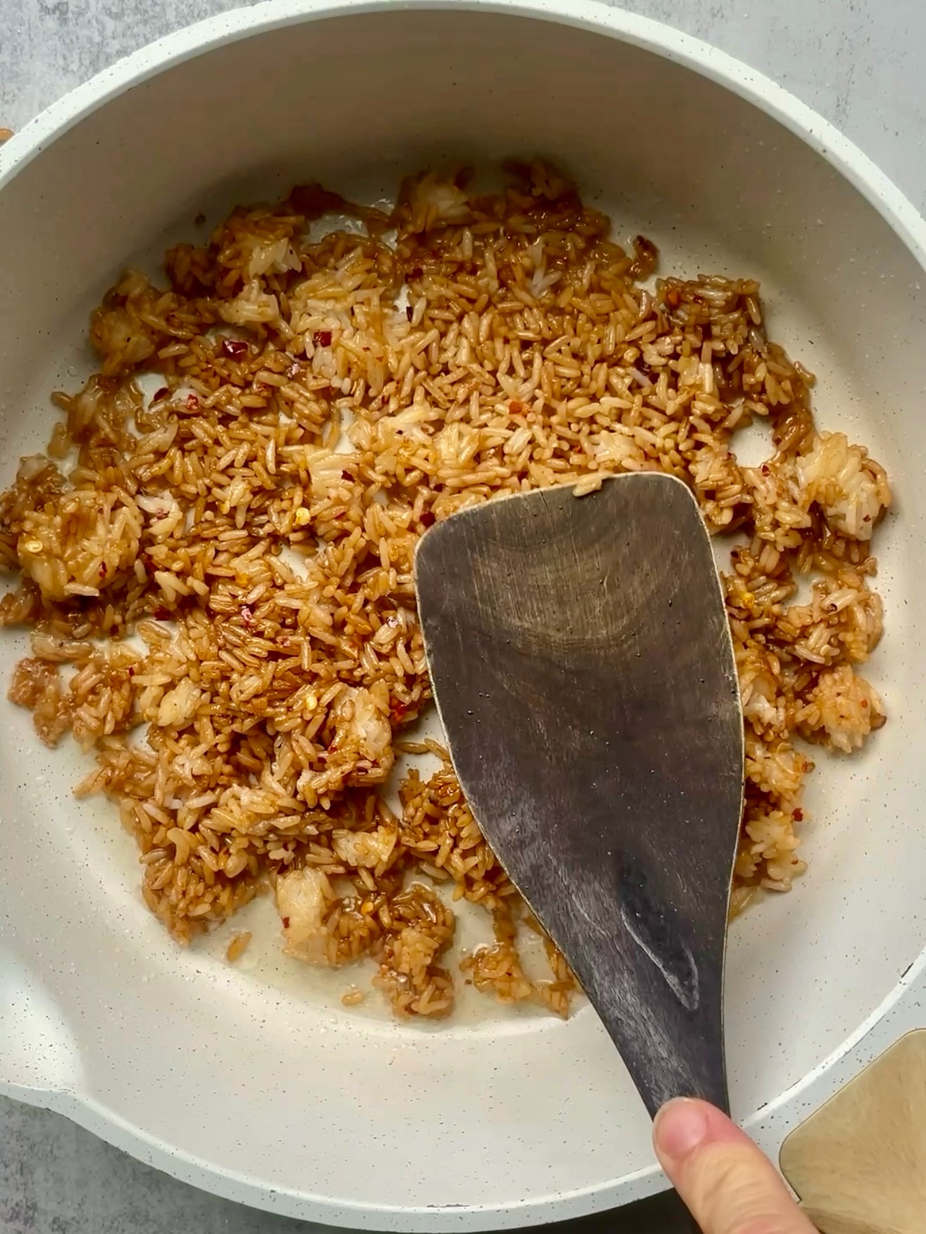 A spatula flipping golden crispy rice in a white skillet.