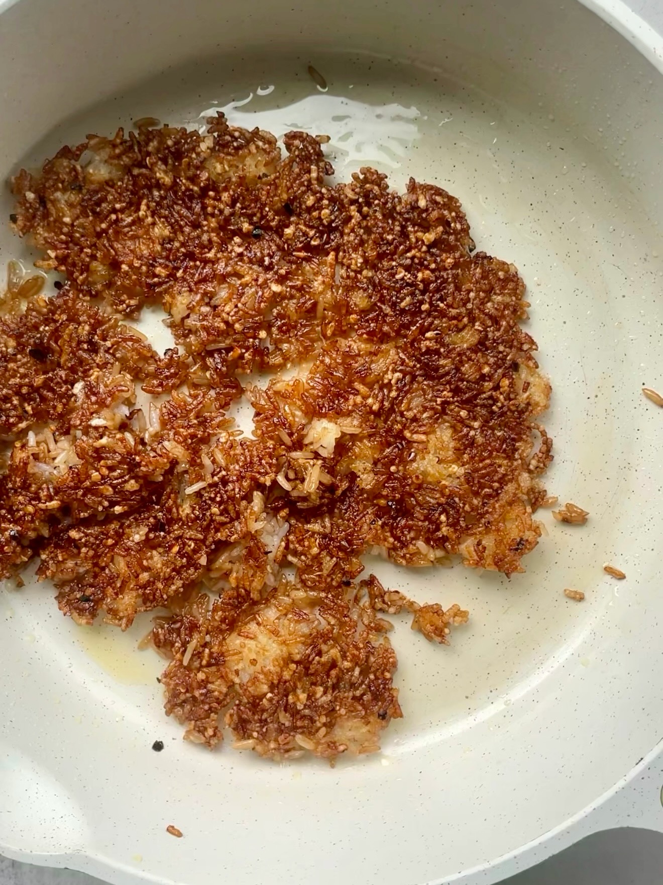 Seasoned rice pressed flat and crisping until golden brown in a skillet.