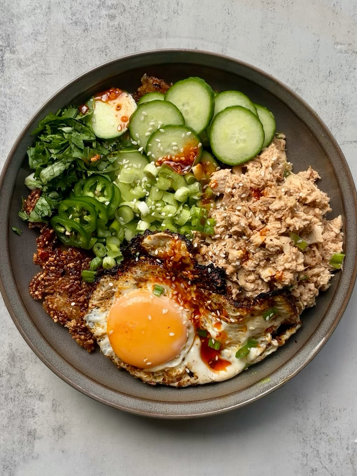 Crispy rice bowl with spicy tuna salad, fried egg, cucumber, jalapeño, green onions, and cilantro.
