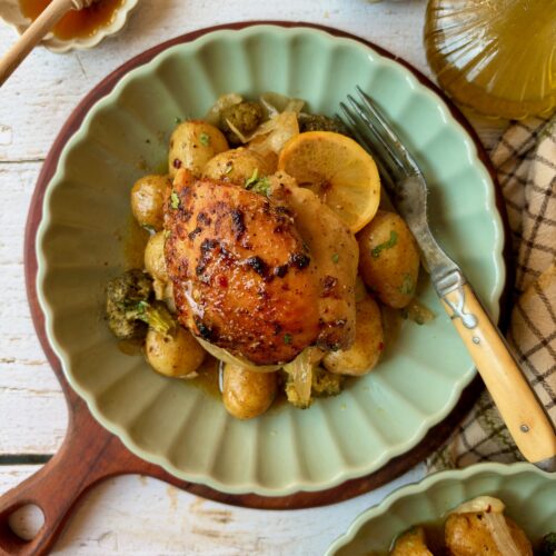 Dump and bake honey mustard chicken thigh served over potatoes and broccoli on a green plate with lemon slices.