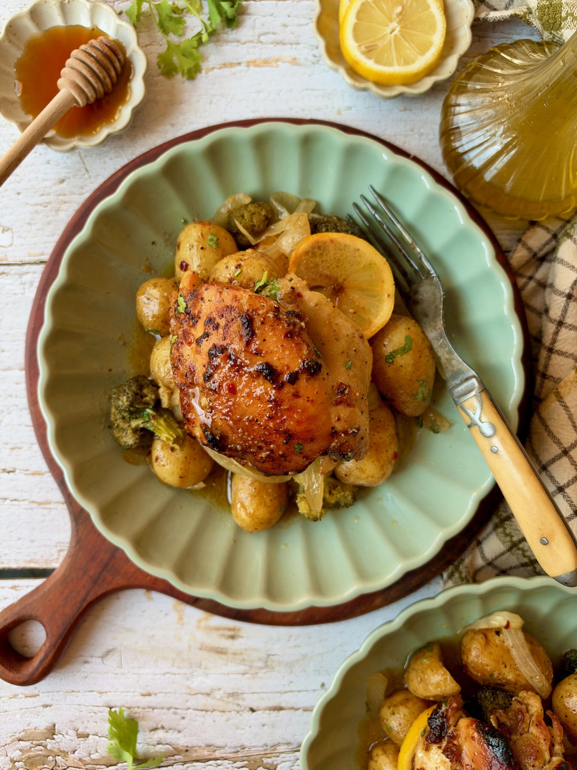 Dump and bake honey mustard chicken thigh served over potatoes and broccoli on a green plate with lemon slices.