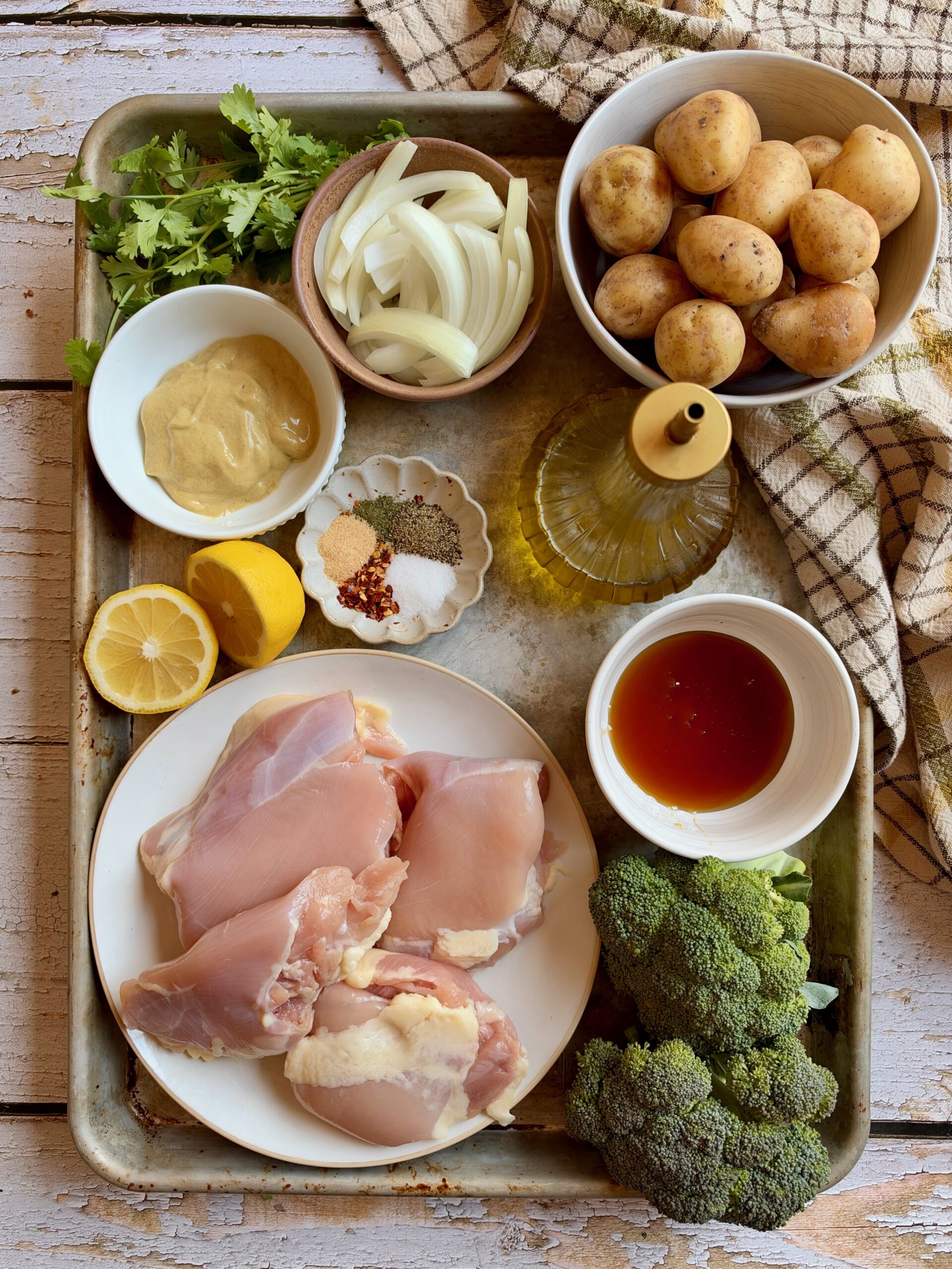 Ingredients for dump and bake honey mustard chicken and potatoes, including chicken thighs, petite gold potatoes, broccoli, onion, Dijon mustard, honey, lemon, olive oil, and spices.