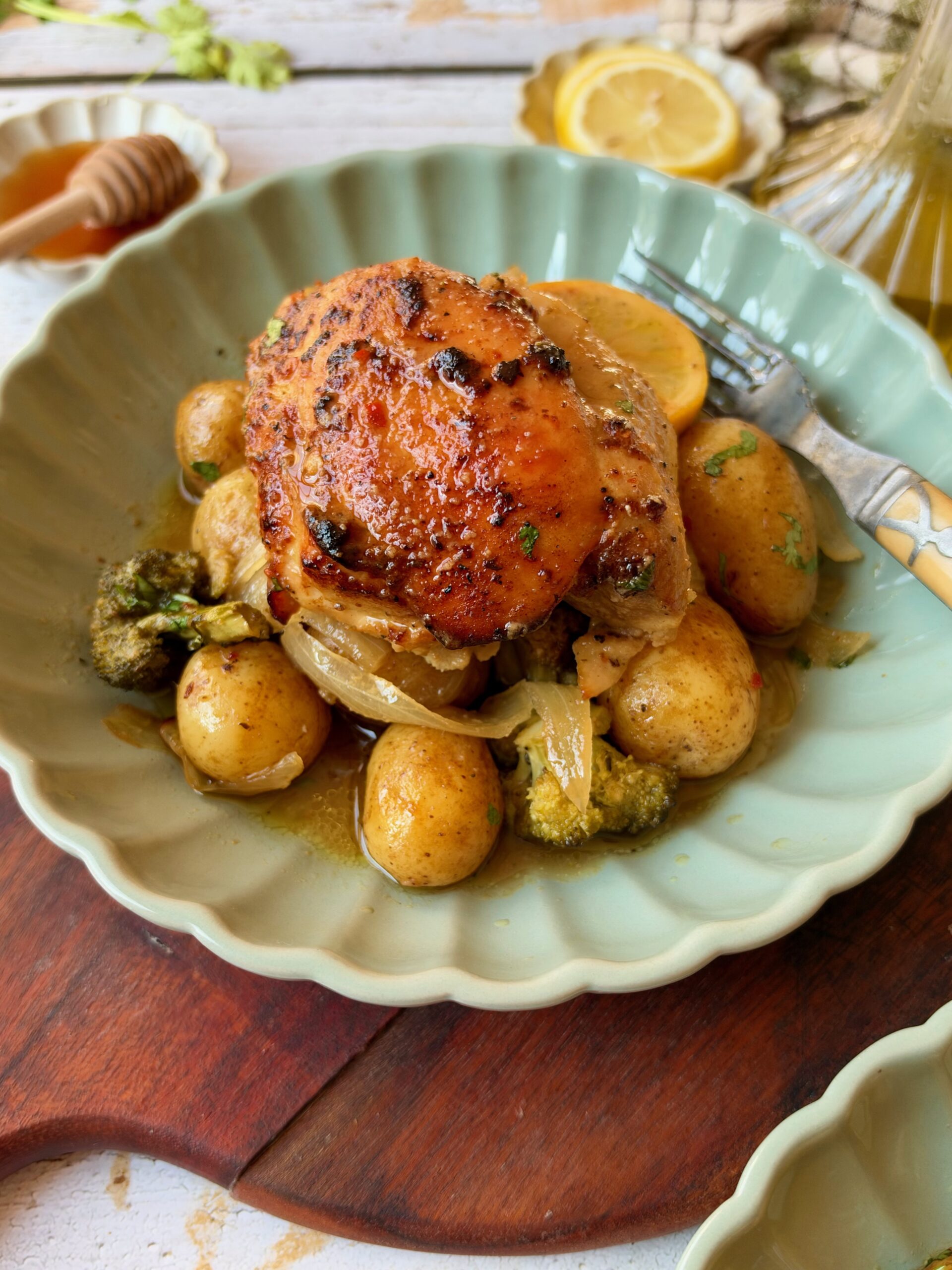 A golden honey mustard chicken thigh with baby potatoes, broccoli, and onion on a green plate.