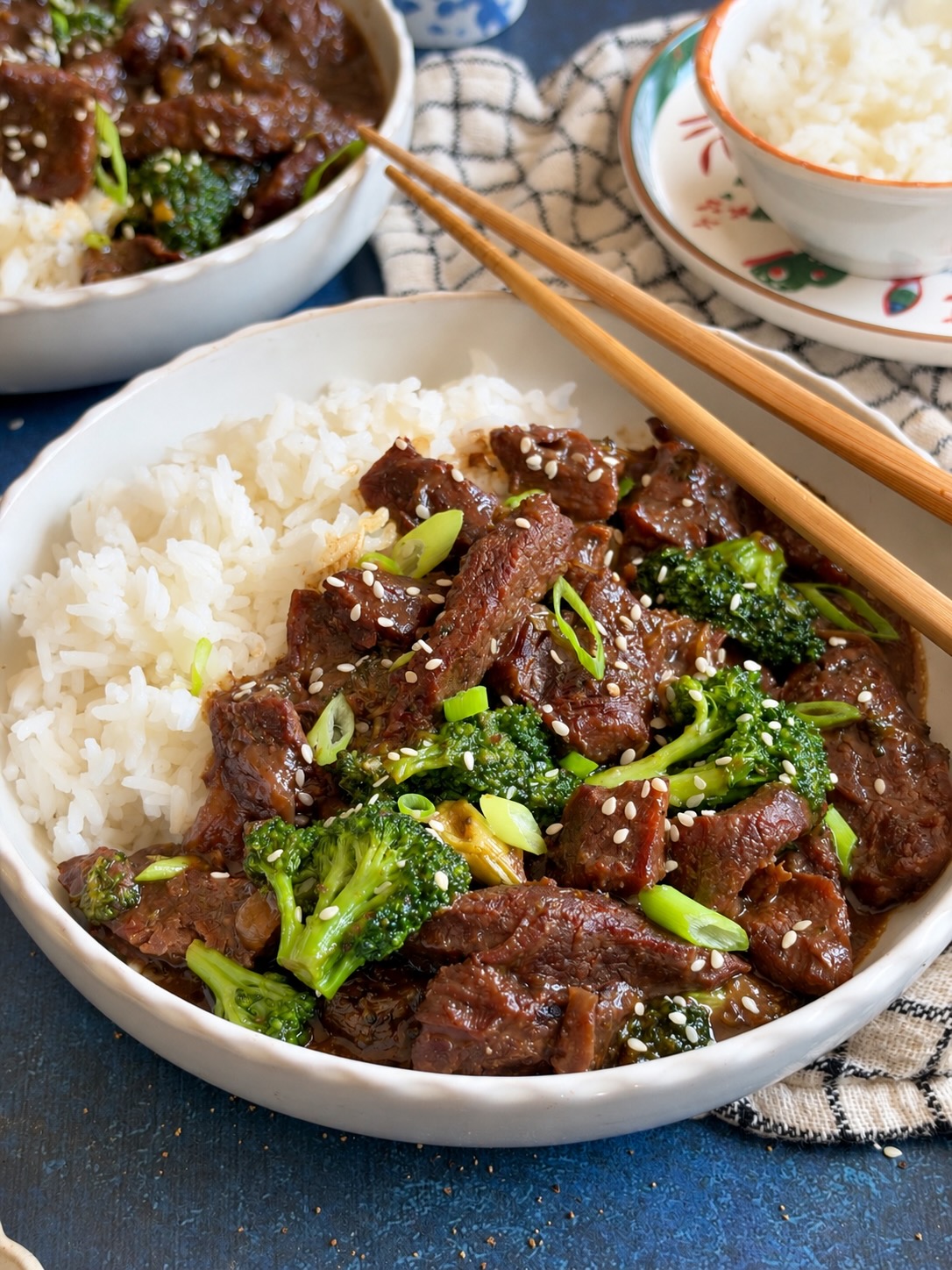 Close-up of Mongolian beef and broccoli over rice in a white bowl with chopsticks.