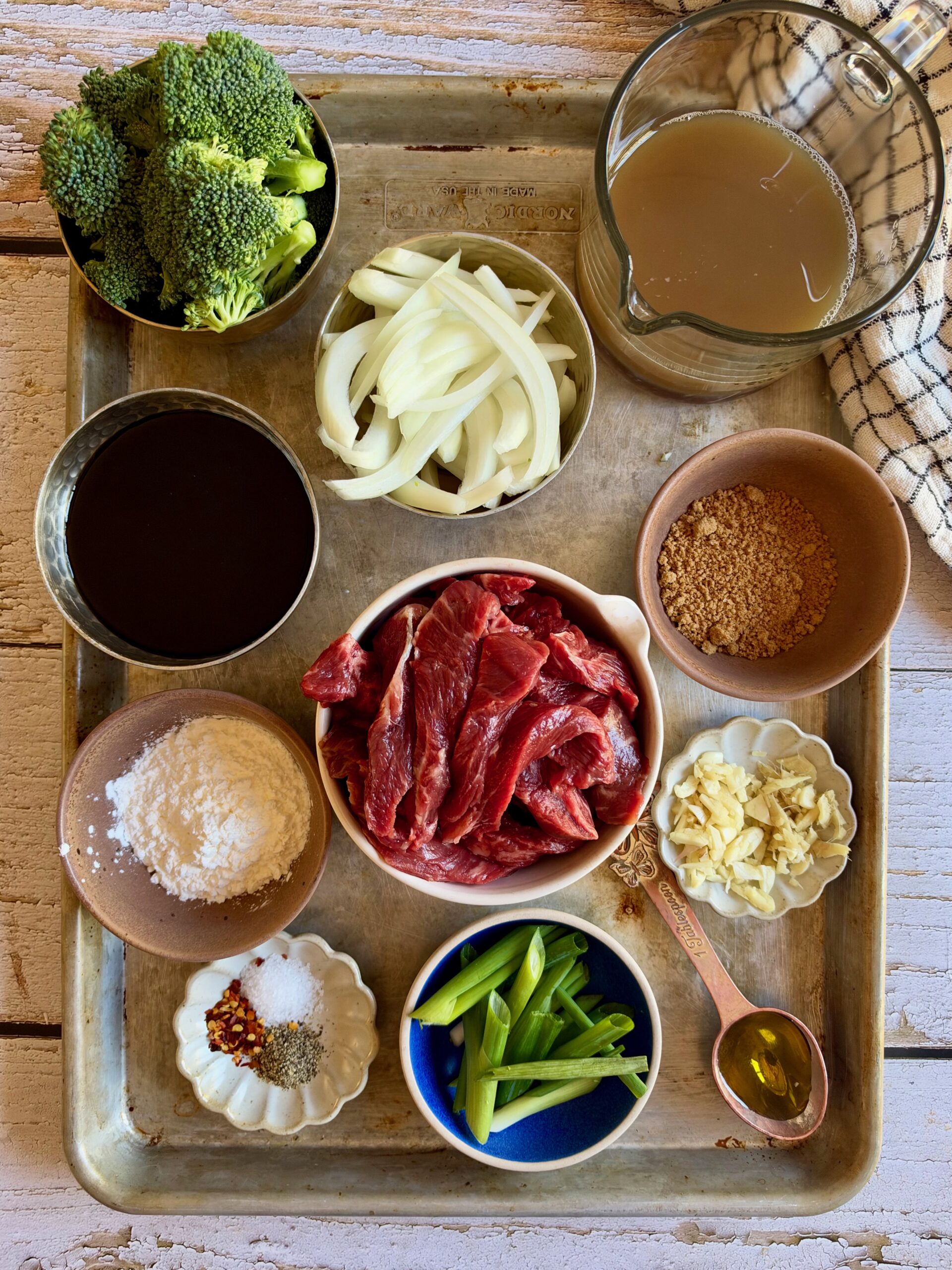 Ingredients for crockpot Mongolian beef and broccoli on a sheet pan, including stew beef, broccoli, onion, green onions, coconut aminos, broth, cornstarch, garlic, and ginger.