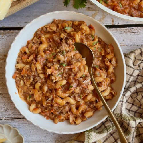 High protein cottage cheese pasta with ground beef in a white bowl with a gold spoon.