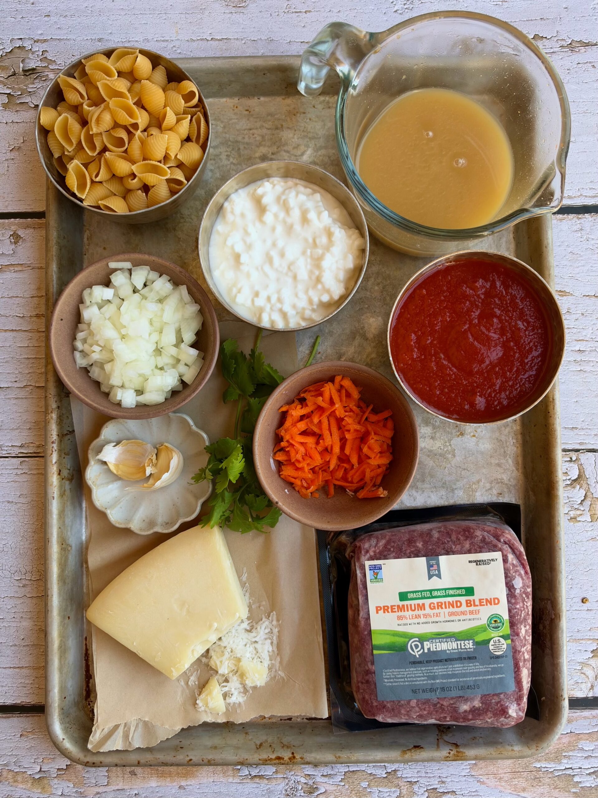 Ingredients for high protein cottage cheese pasta on a sheet pan, including pasta, cottage cheese, broth, marinara, onion, garlic, grated carrot, Parmesan, and ground beef.