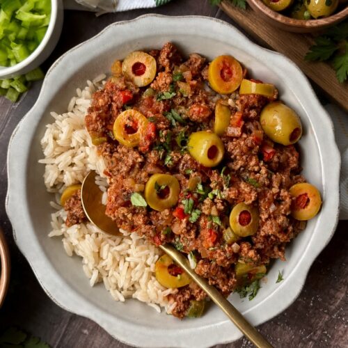Picadillo with green olives served over white rice in a white bowl with a gold spoon.