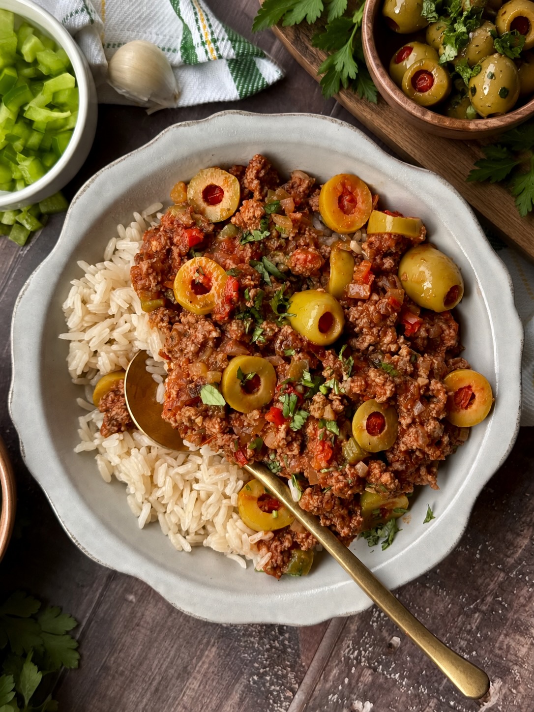 Picadillo with green olives served over white rice in a white bowl with a gold spoon.