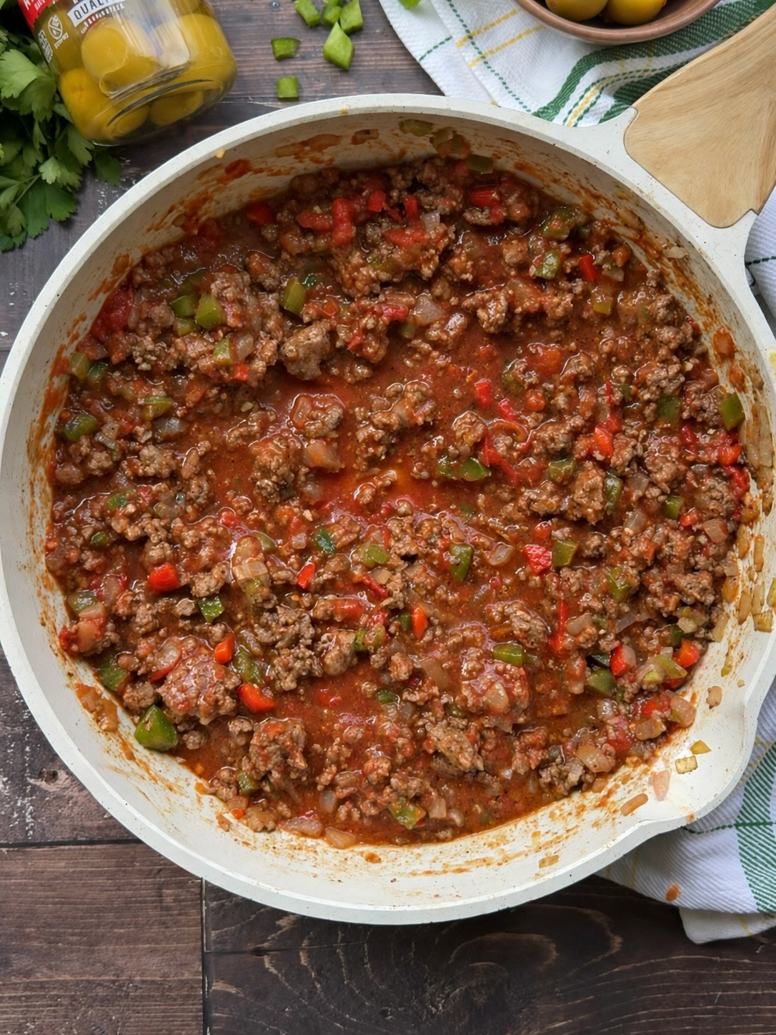 Ground beef picadillo simmering in tomato sauce with bell peppers in a white skillet.