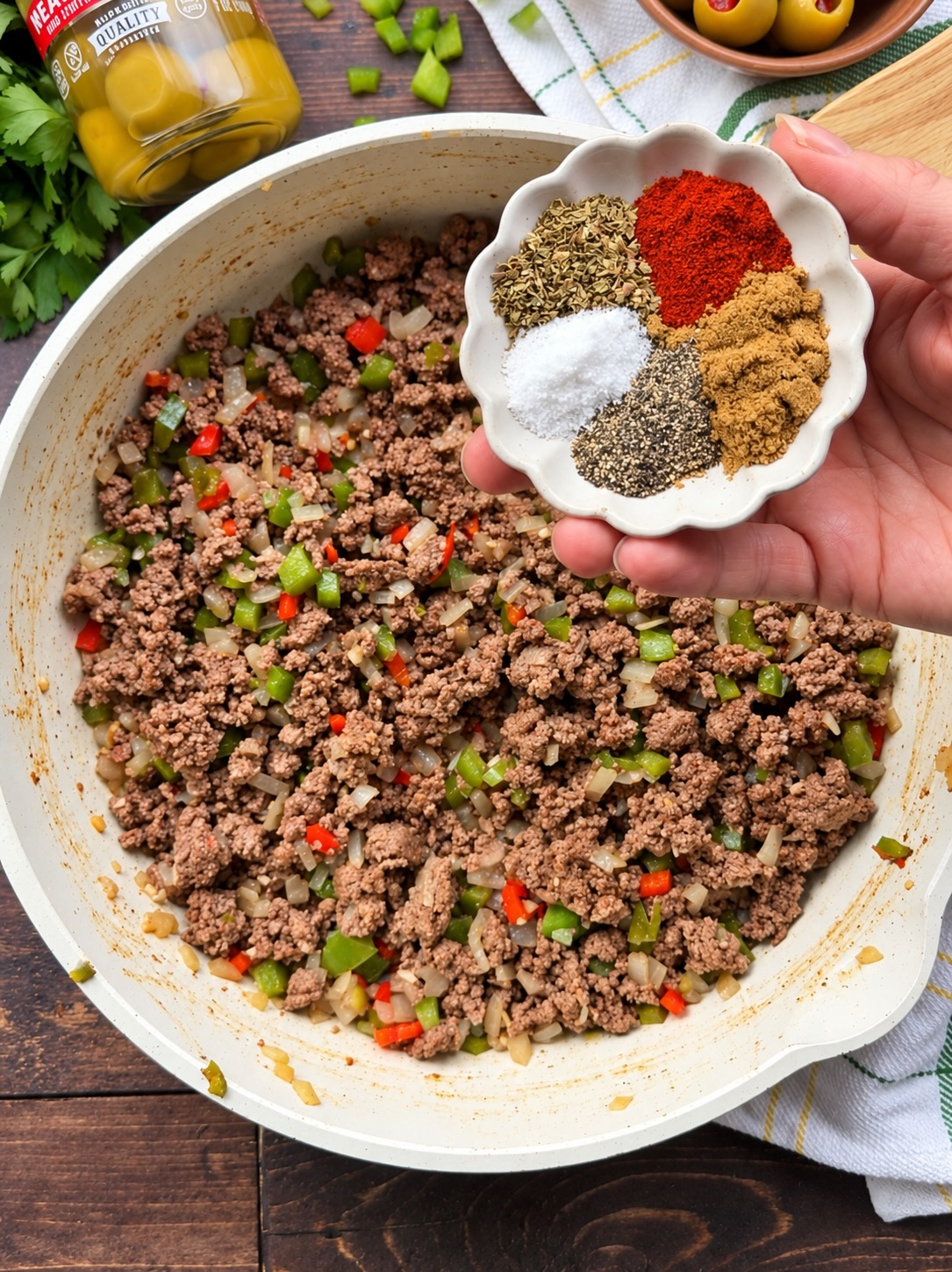 Cumin, oregano, paprika, salt, and pepper being added to browned ground beef and peppers in a skillet.