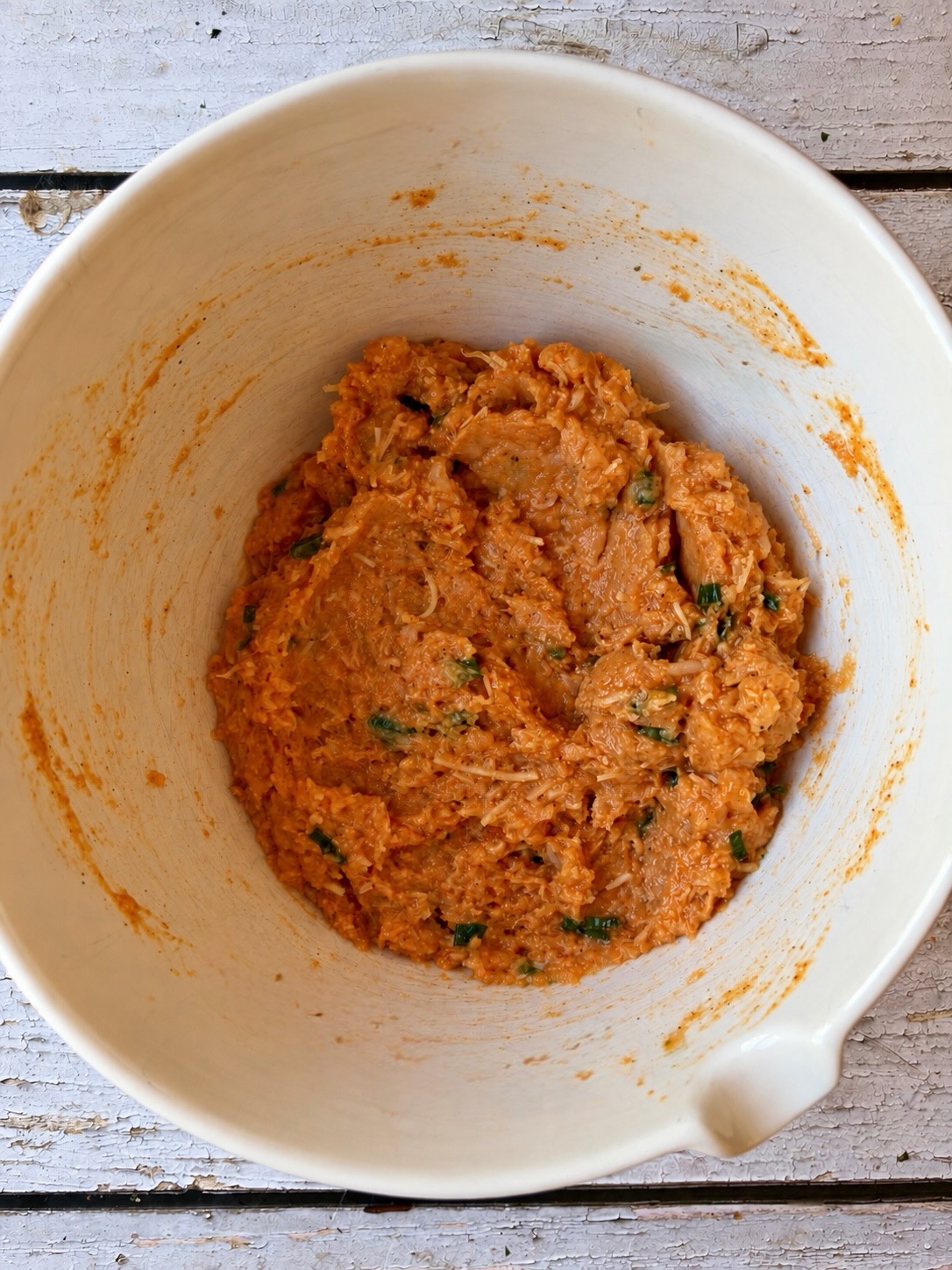 Ground chicken mixed with buffalo sauce, mozzarella, green onions, and spices in a white bowl.