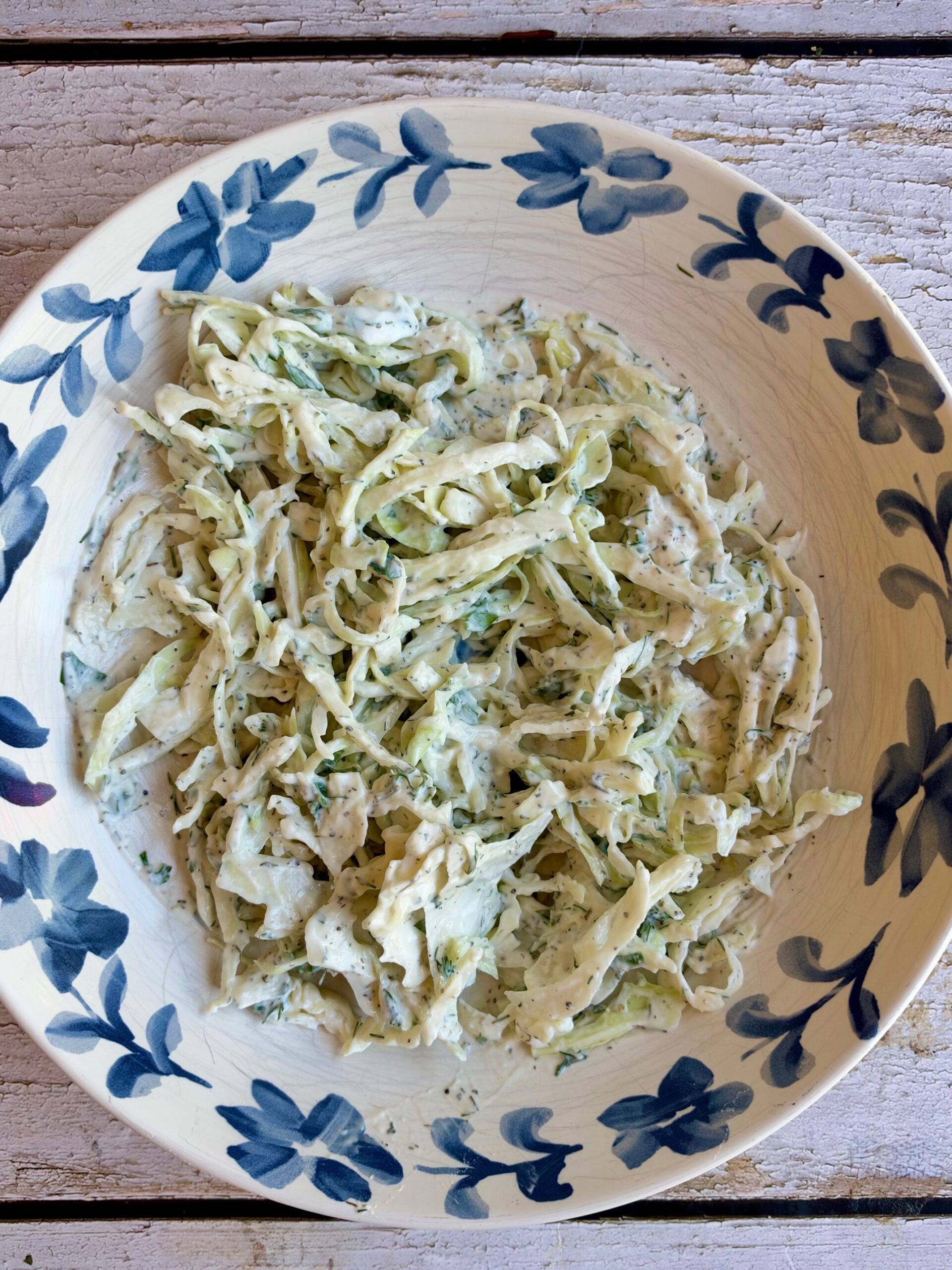 Creamy Greek yogurt dill slaw with shredded cabbage in a blue and white bowl.