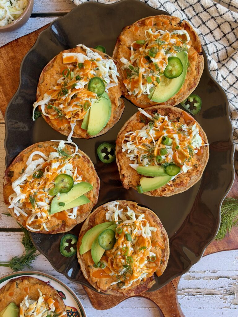Buffalo chicken smash tacos topped with dill slaw, avocado, jalapeño, and buffalo sauce on a serving platter.