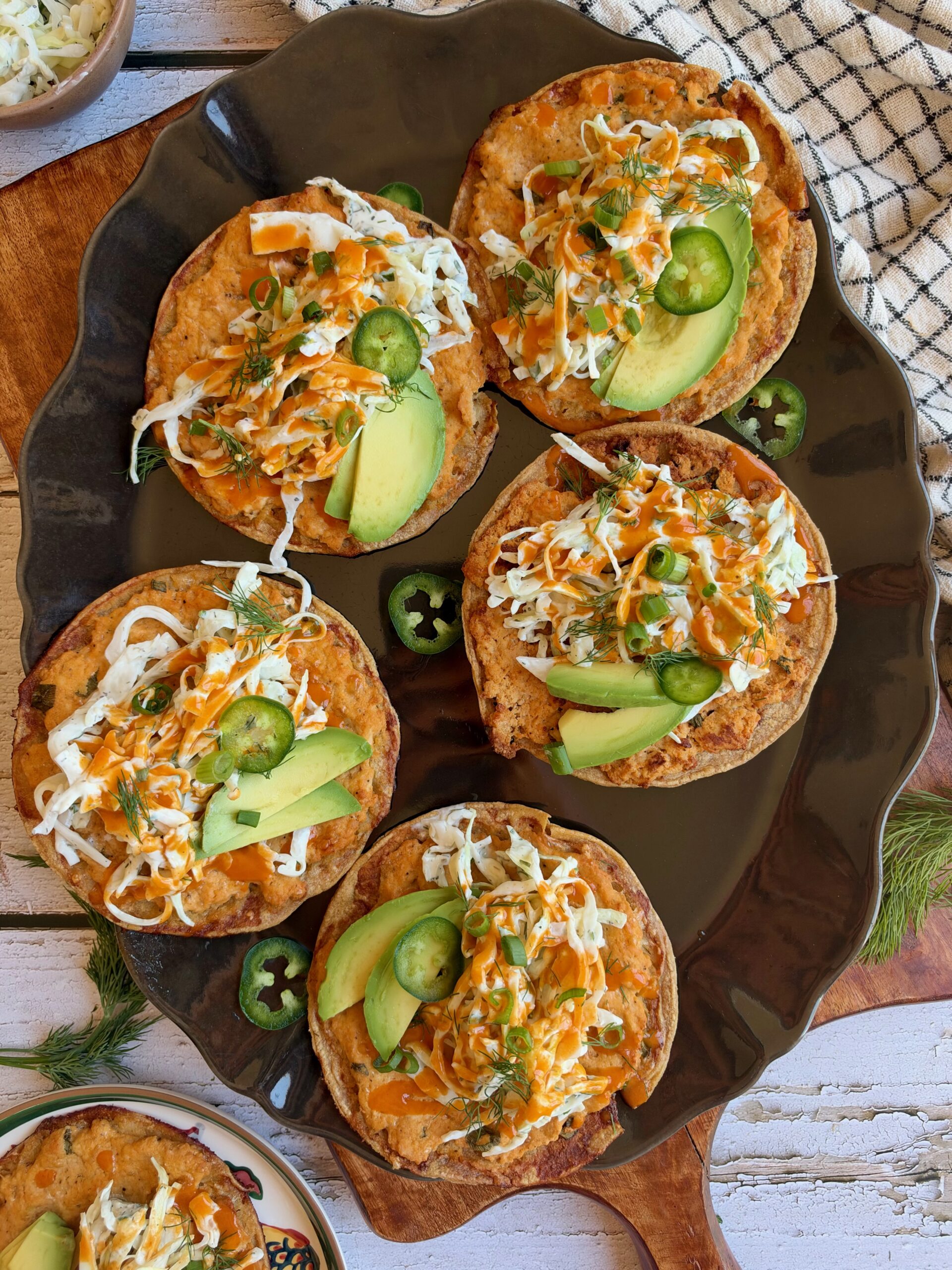 Buffalo chicken smash tacos topped with dill slaw, avocado, jalapeño, and buffalo sauce on a serving platter.