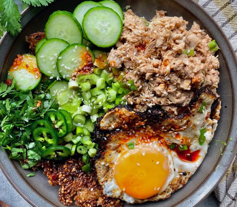 Spicy tuna crispy rice bowl topped with a fried egg, cucumber, jalapeño, green onions, cilantro, and chili crisp.