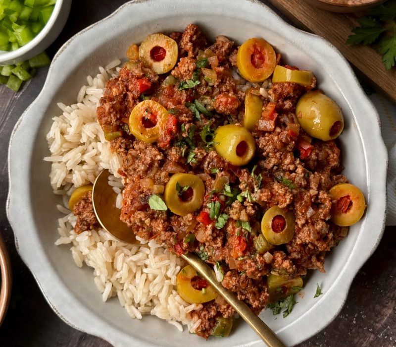 Picadillo with green olives served over white rice in a white bowl with a gold spoon.