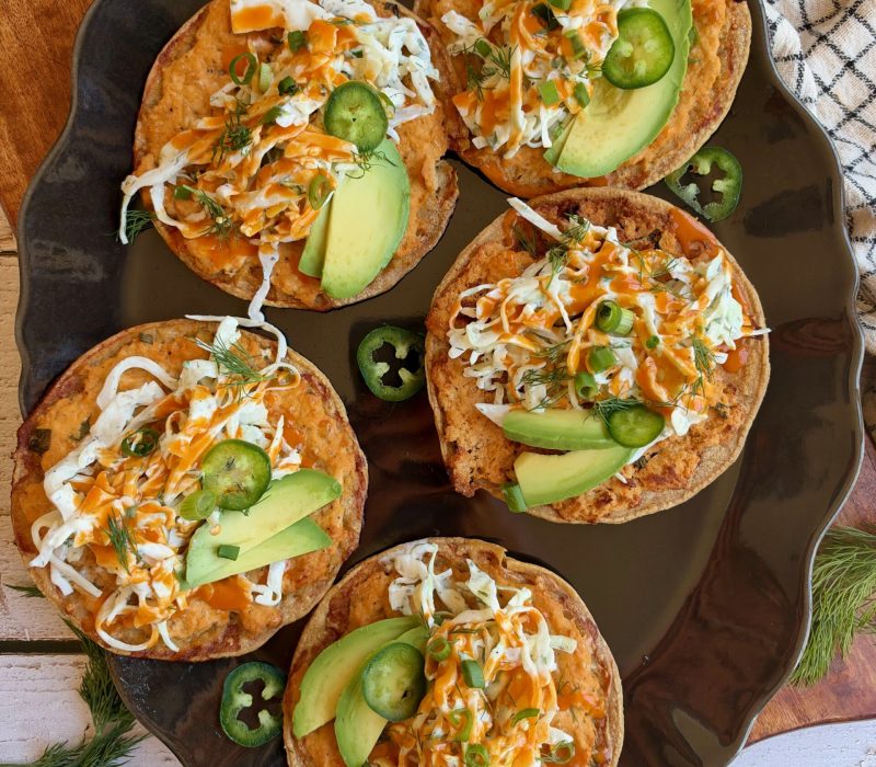 Buffalo chicken smash tacos topped with dill slaw, avocado, jalapeño, and buffalo sauce on a serving platter.